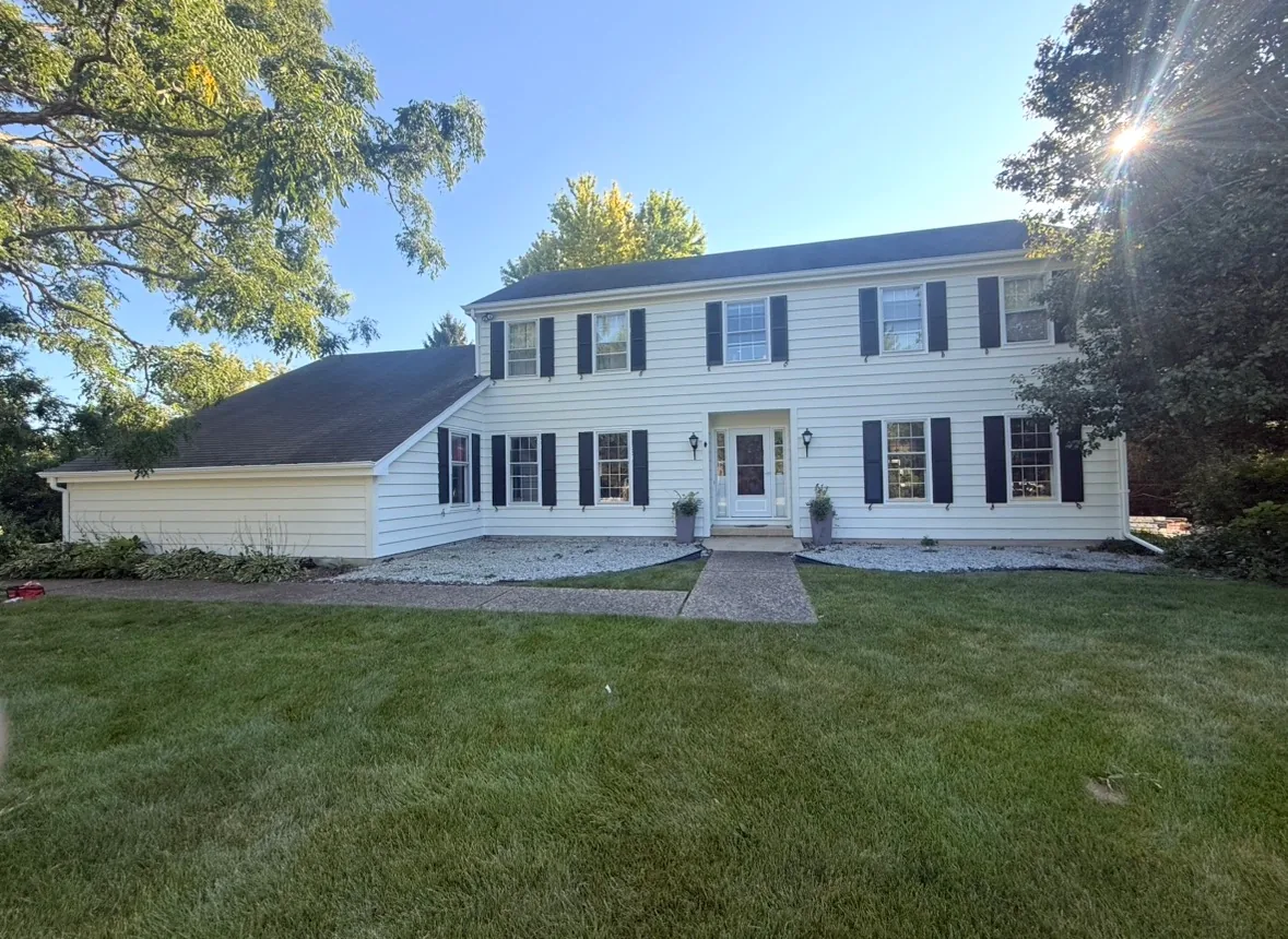 A two-story colonial home with white painted siding and trim, black shutters, a white front door under a small portico, and a mown lawn with a concrete path to the entry.